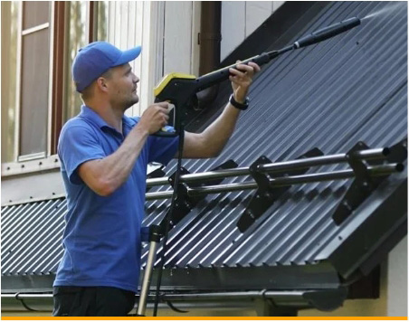 Man cleaning metal roof with power washer